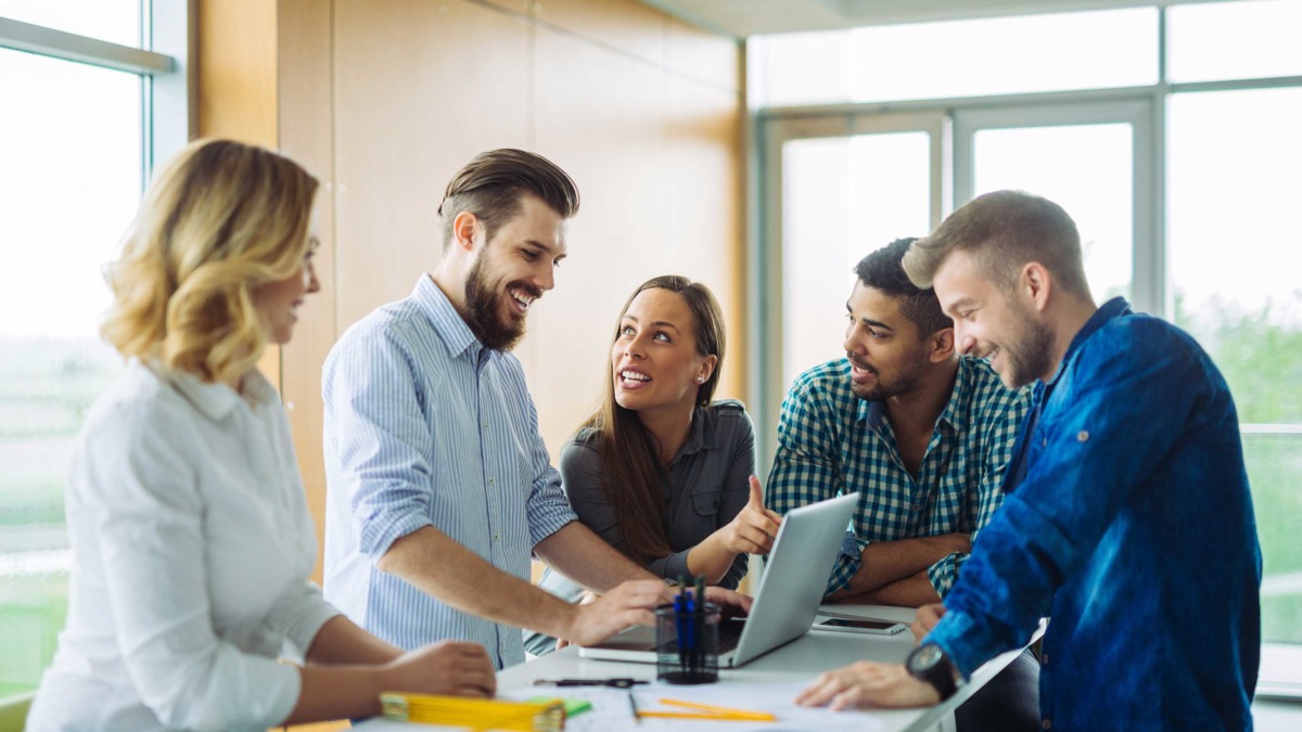 Group of happy young people stood around a laptop discussing work