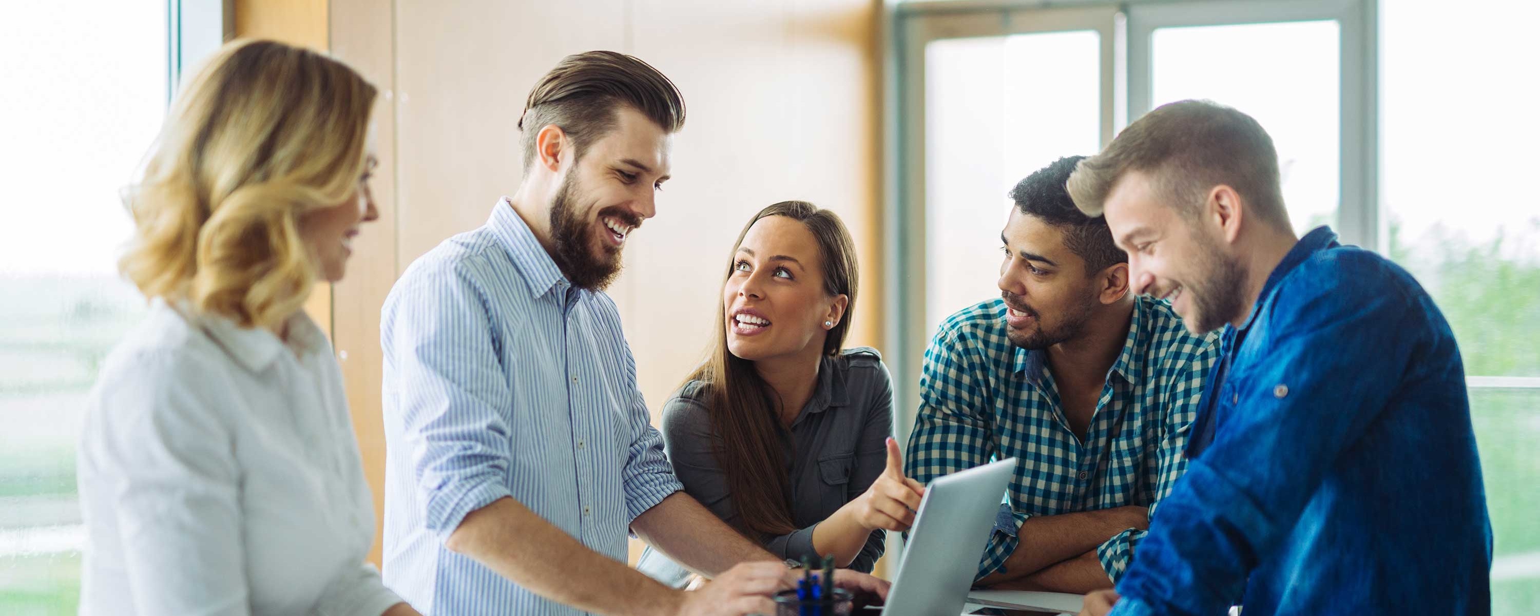 Group of happy young people stood around a laptop discussing work