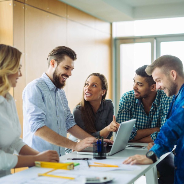 Group of happy young people stood around a laptop discussing work